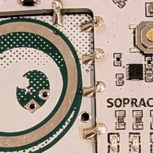 Close-up of a properly soldered castellated edge joint, solder sloping down to the badge pad